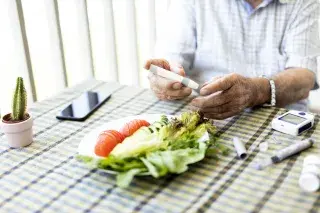 Senior using a glucose meter to get his blood sugar level during a meal