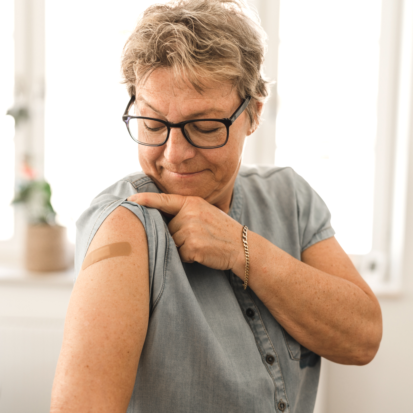 A woman looking at a bandaid on her upper arm