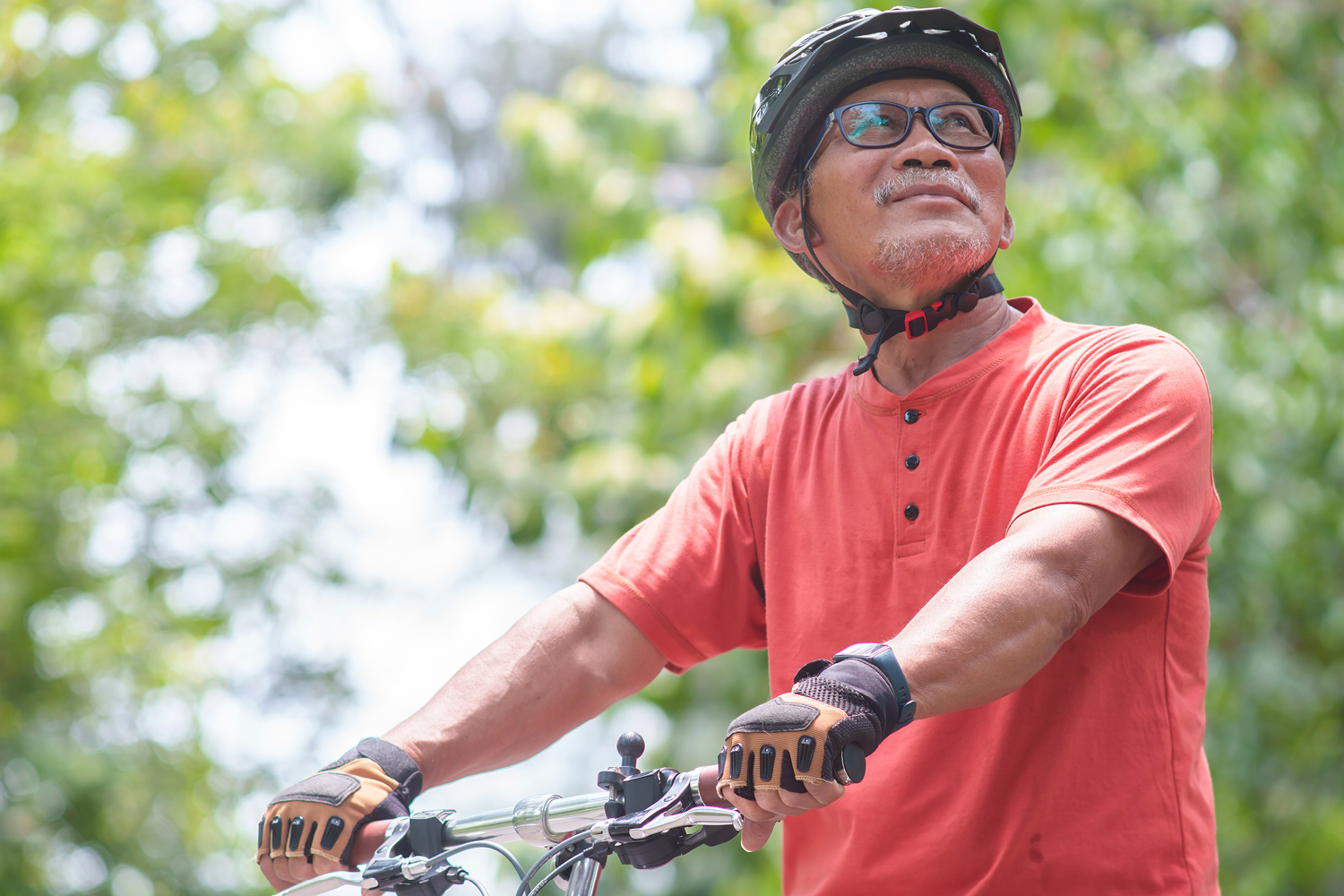 A man in an orange shirt cycling through a park