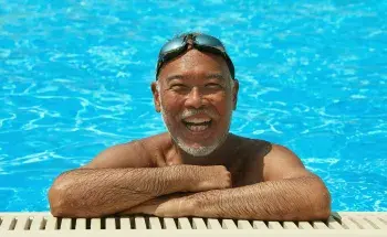 A smiling older man at the edge of a swimming pool