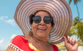Smiling older woman with a sunhat against a background of palm trees and blue sky