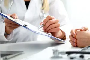A doctor talking with a patient and pointing to something on a clipboard