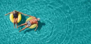 Overhead view of an older man and woman floating in a pool and holding hands