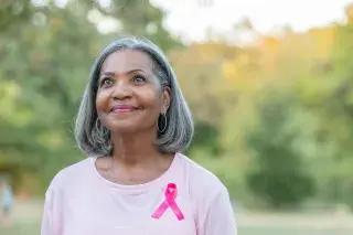 A senior smiling while wearing pink and a breast cancer ribbon