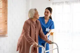 Elderly women walking assisted by a walker and nurse