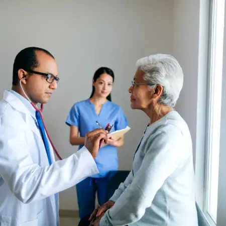 A doctor examining his older patient, assisted by a member of the care team