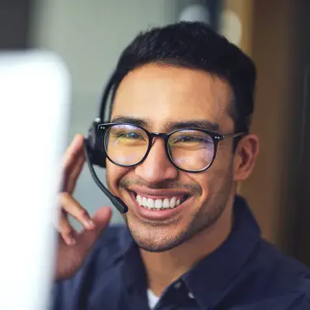 A smiling man wearing a headset and looking at a computer screen